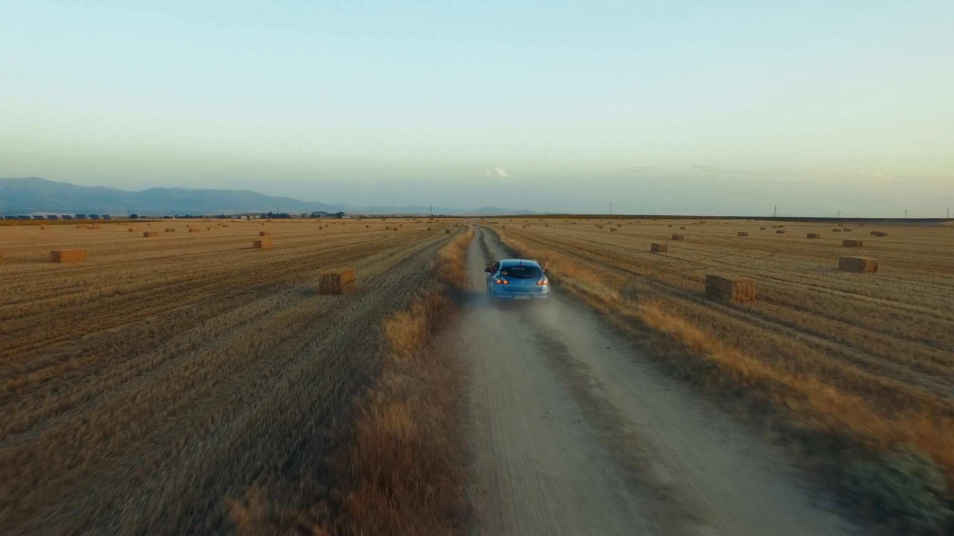 A car driving between fields at sunset